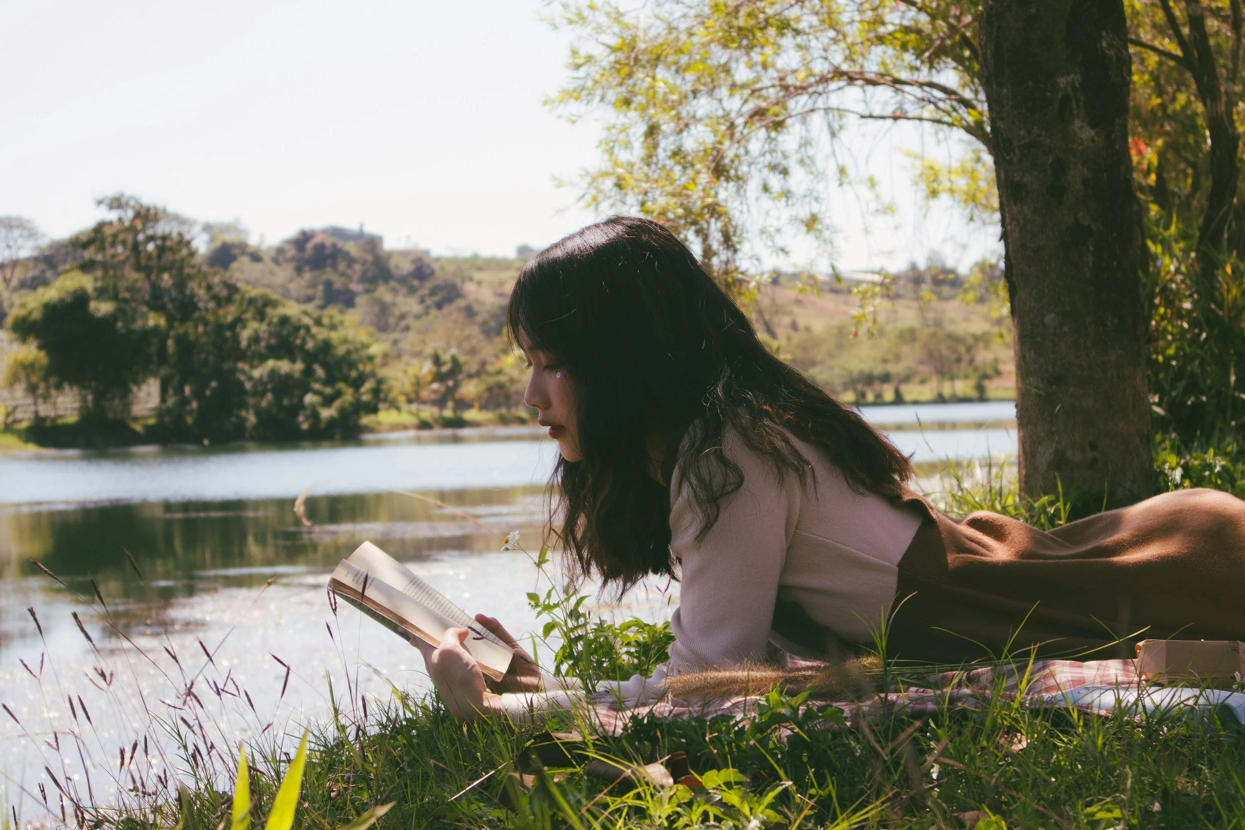 Person reading by a tranquil lakeside.
