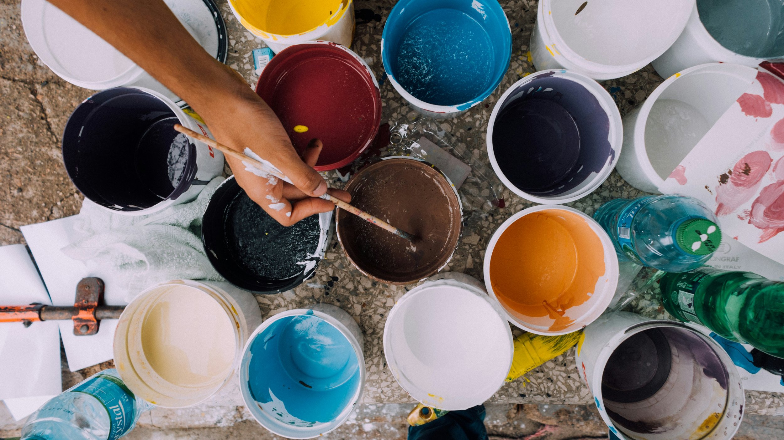 Hand stirring paint in various color buckets.