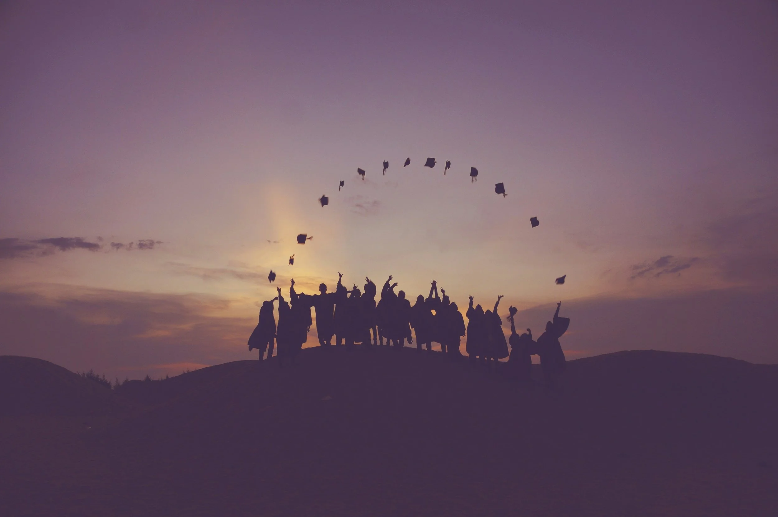 Graduates celebrating at sunset with thrown caps.