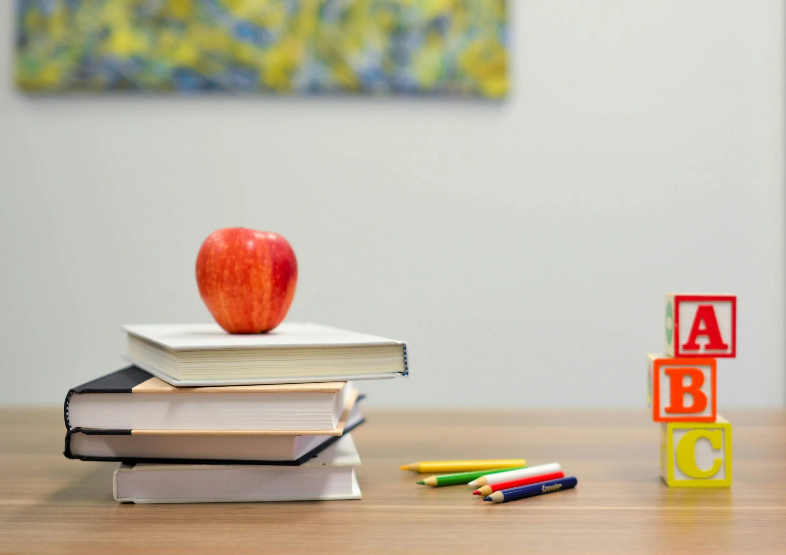 An apple atop stacked books and colorful pencils.