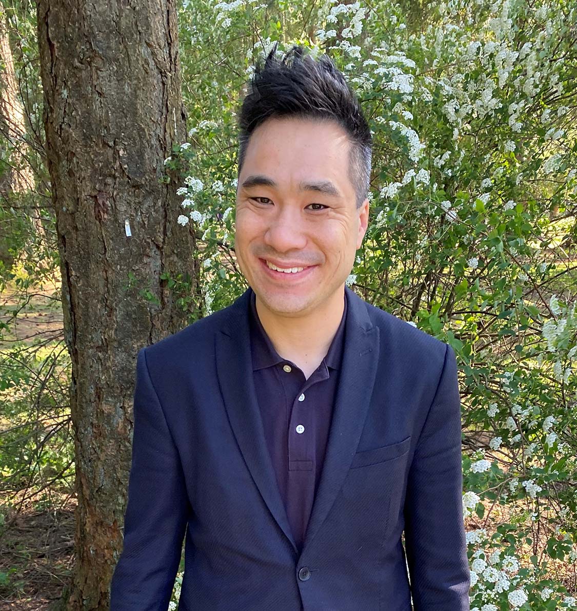 Person smiling outdoors among blooming flowers.